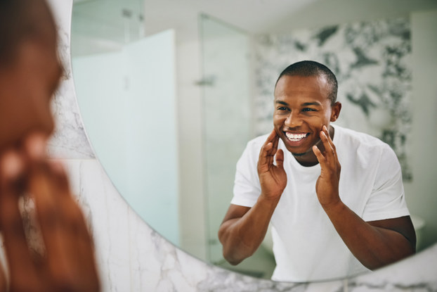 man looking in mirror touching his face