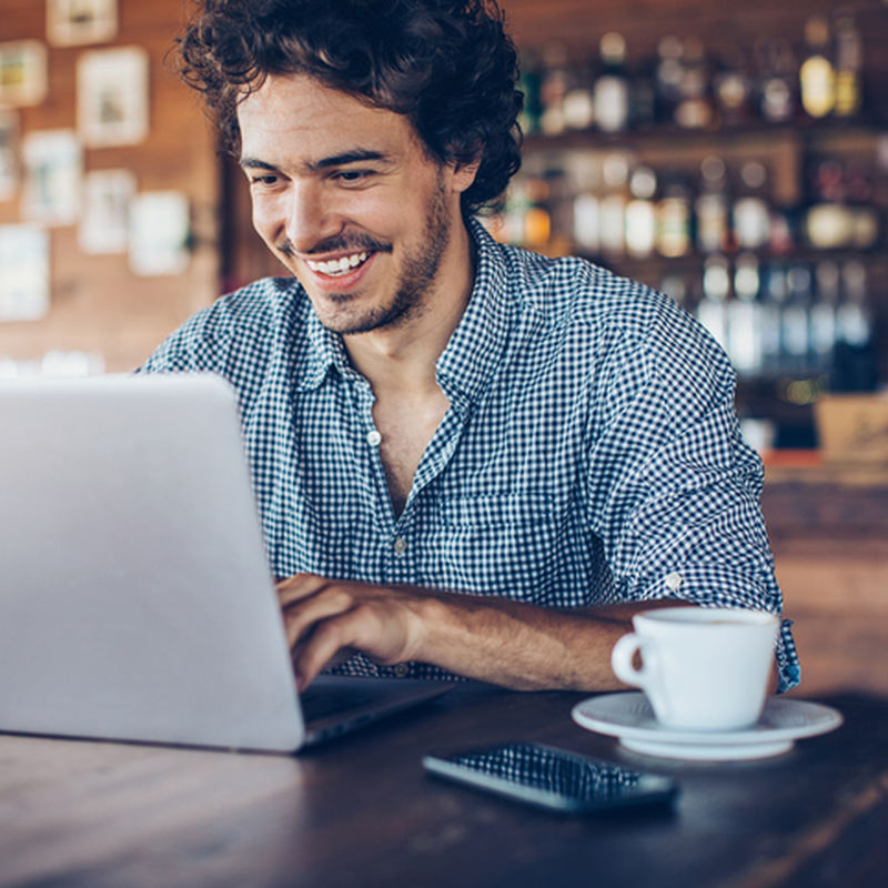 man smiling at laptop in a coffee shop