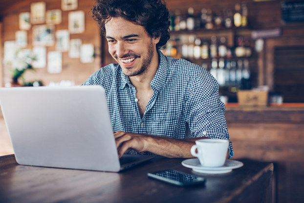 man smiling at laptop in a coffee shop
