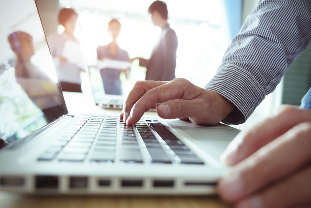 man on laptop with coworkers in the background