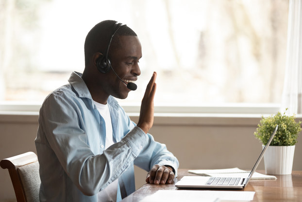 man working remotely waving to laptop screen