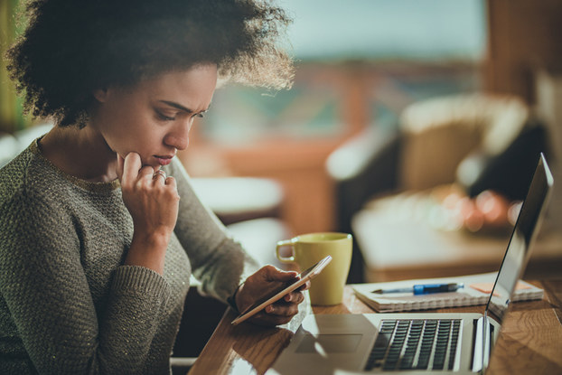woman sitting with laptop and looking at phone