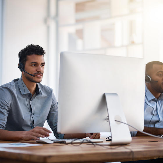 two male coworkers with headsets on laptops