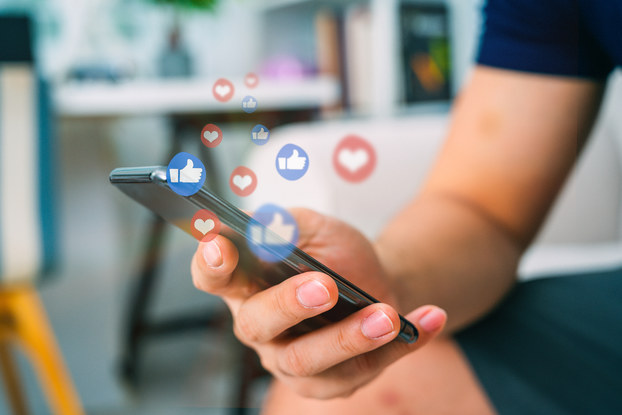 person holding cell phone with social media icons floating above
