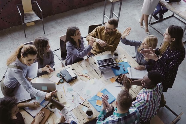 Overhead photo of employees high fiving at work table