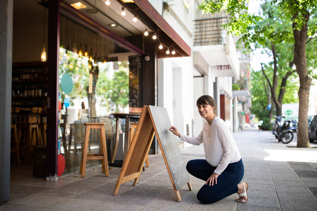 woman outside shop writing on chalkboard