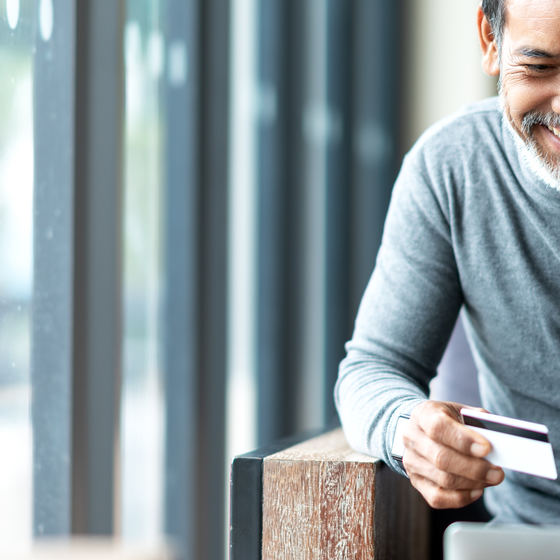 A man holding a credit card shops on his laptop.