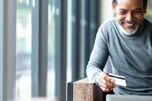 A man holding a credit card shops on his laptop.