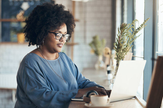 A woman works on her laptop near a window.