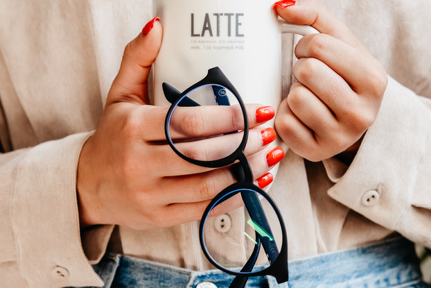 woman holding blenders sunglasses and coffee mug