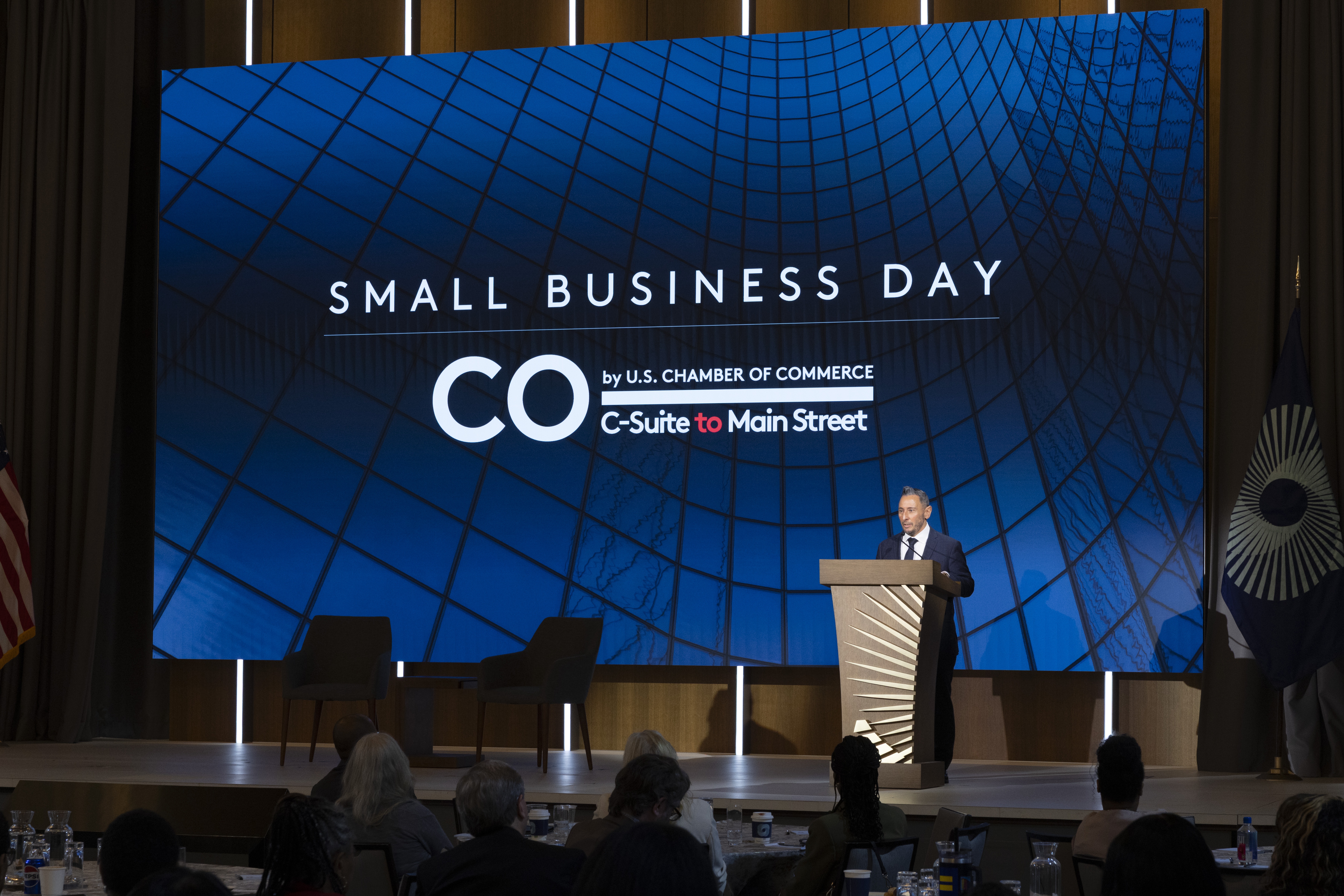 a man standing at a podium with a large screen behind him