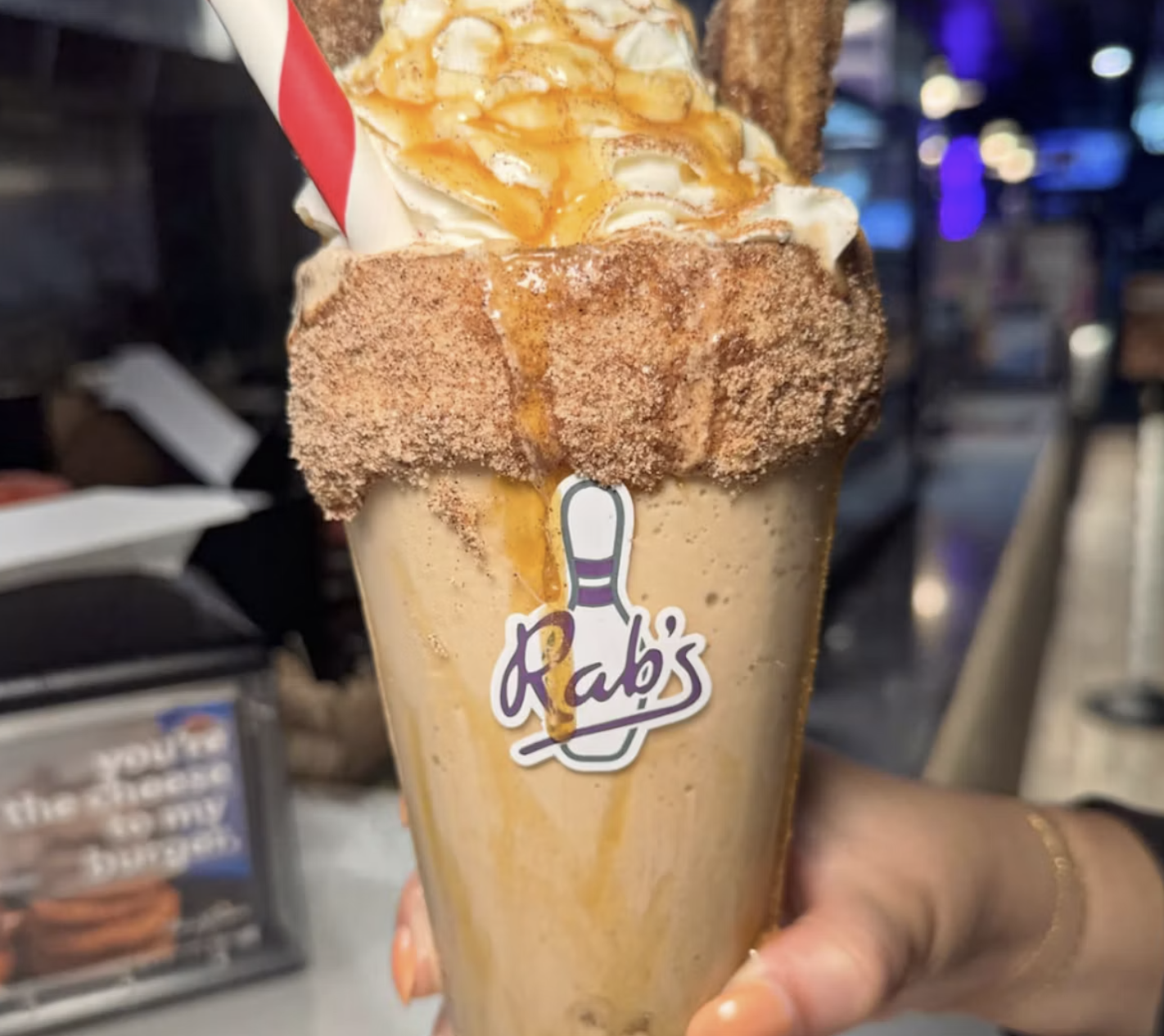 a hand holding a milkshake with the Rab's Country Lanes bowling pin logo on the glass