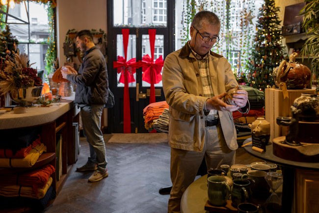 A male customer holds up a ceramic jar. In the background is a small retail shop decorated with holiday decor.