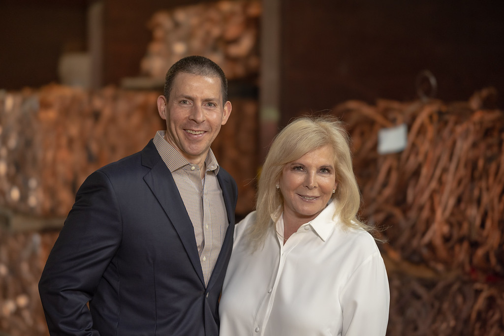 United Scrap Metal Founders, Brad and Marsha Serlin, standing together in front of piles of scrap metal shredded into long strips.