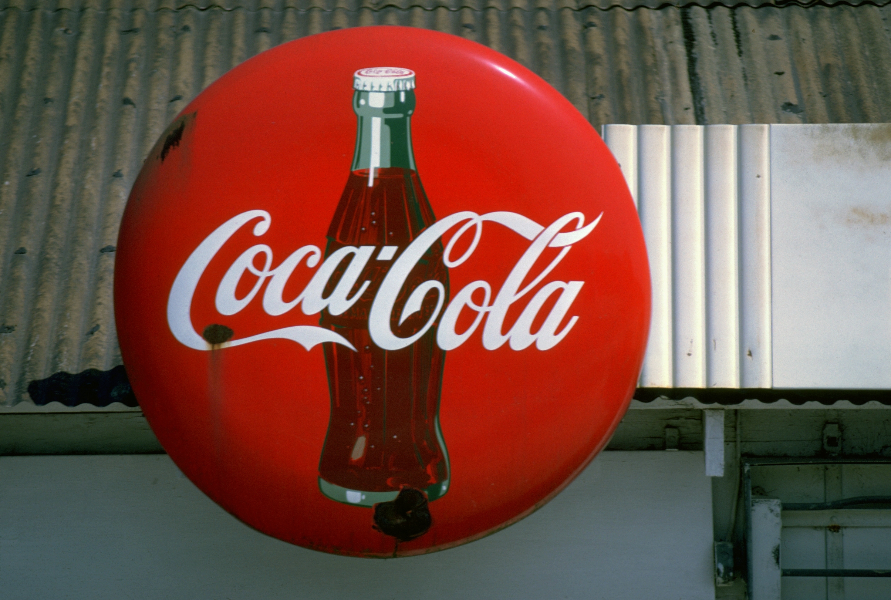 A red, round Coca-Cola sign hanging on a building.