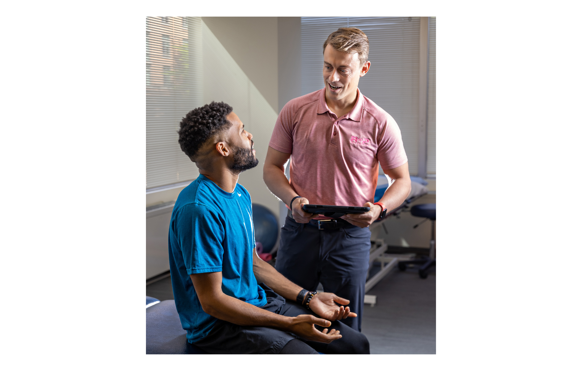 A physical therapist talking to a patient sitting on a couch.