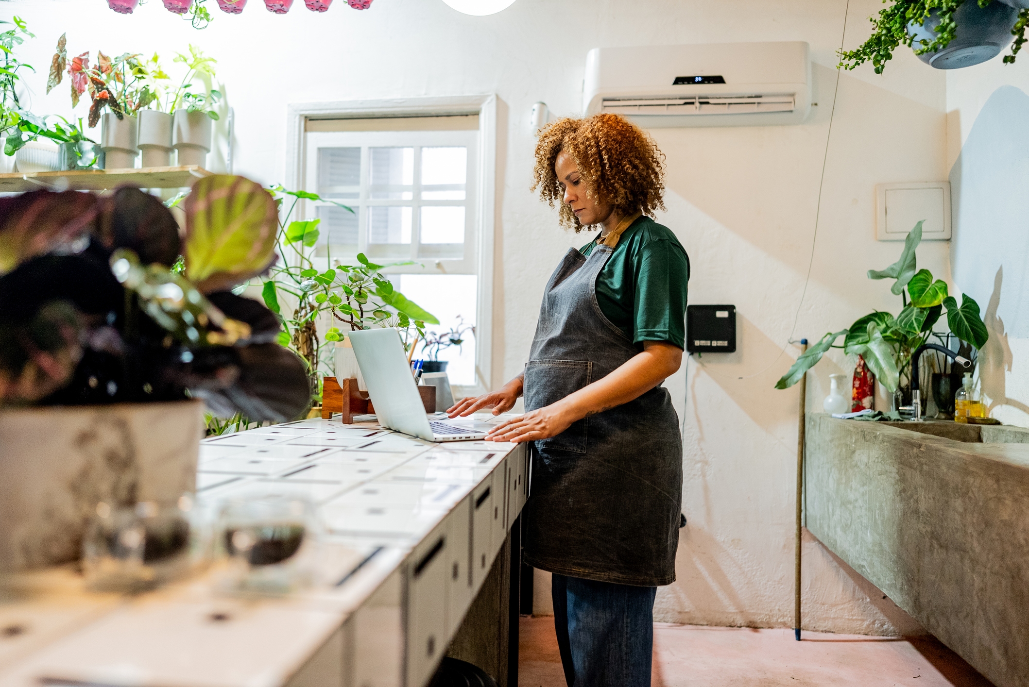 A woman business owner standing in front of a laptop inside her plant shop.
