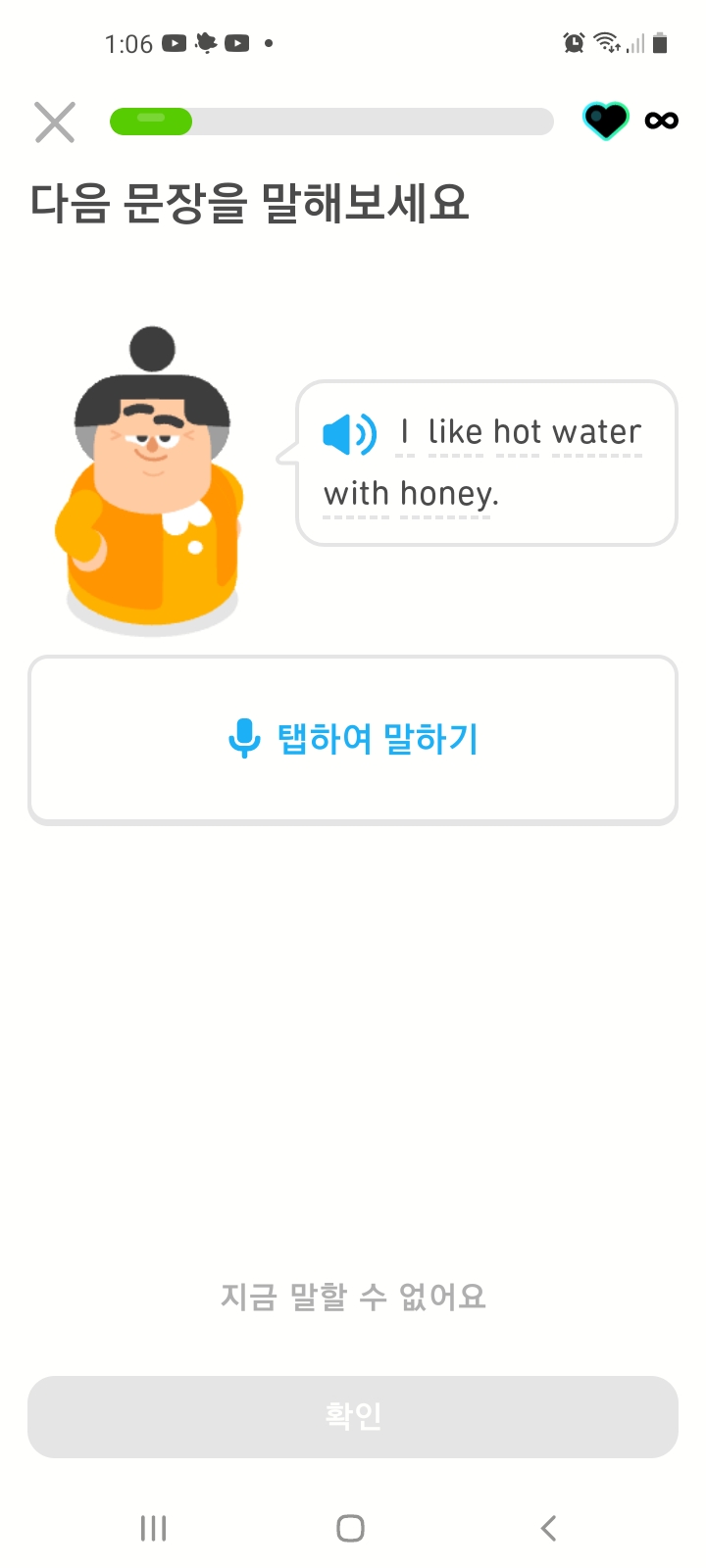 말하기 연습문제를 보여주는 스크린샷. 앱 화면에 루시가 있고 그 옆 말풍선에 “I like hot water with honey.”라고 써 있다. 그 아래 파란 마이크 버튼을 “탭하여 말하기” 하는 연습문제이다.