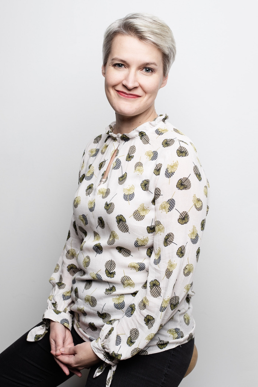 Sopraano Laura Pyrrö, vaaleat hiukset, ystävällinen hymy, punainen esiintymismekko ja valkoinen bolero.