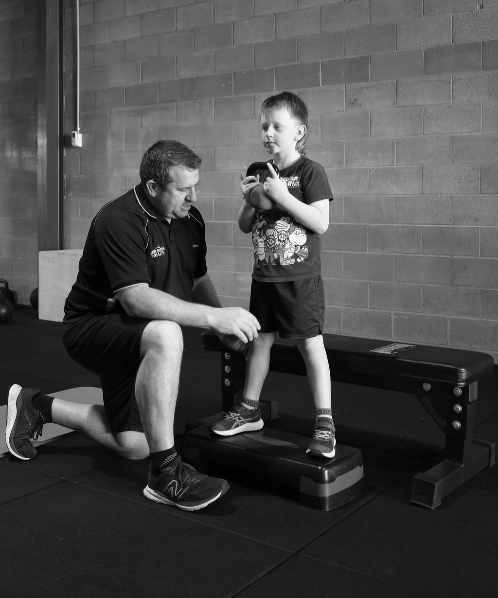 Fitness Classes for Kids and Young Athletes in Dubbo Man Coaching a young boy who is holding a kettlebell, standing on a step