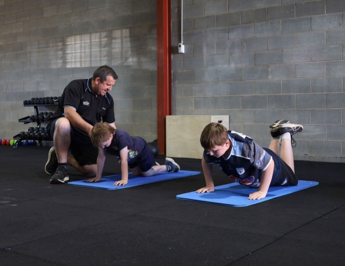 Youth Strength and Conditioning Classes in Dubbo Man coaching two young males on how to perform a push up in a gym
