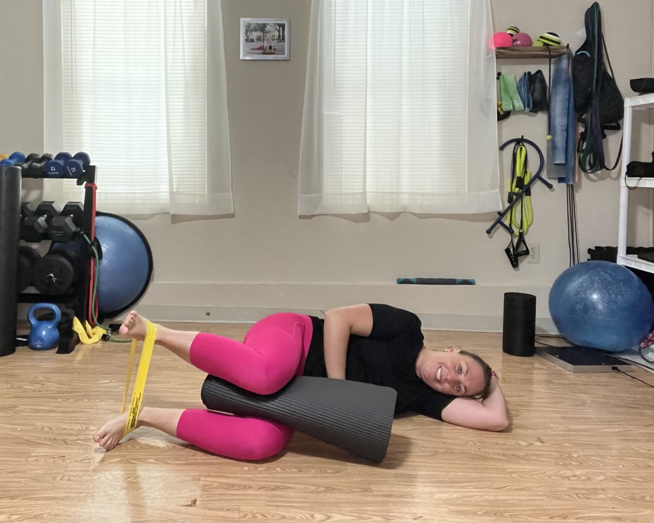 A women laying on her side with a yoga mat between her knees and a yellow band around her ankles