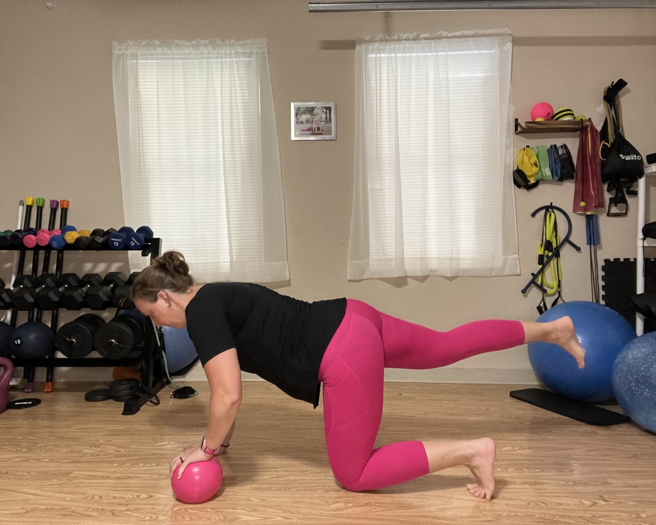 A female in hands and knees with a ball under one hand and the opposite leg raised and straight
