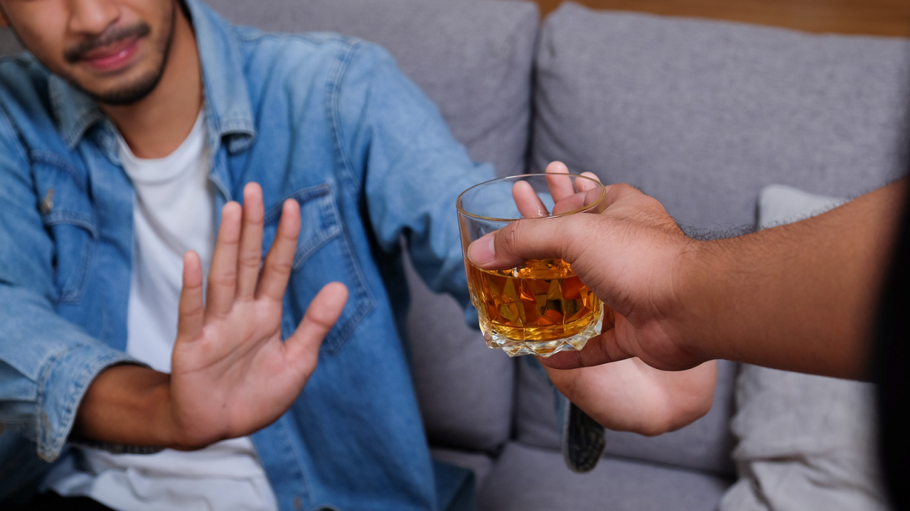A person holding a glass of alcohol but deciding not to drink it, as they recognize it as a trigger for their condition.