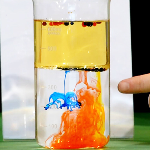 Food colouring dropping thrugh vegetable oil and water, with colourful explosions of food colouring the water at the bottom of the glass> <div class=