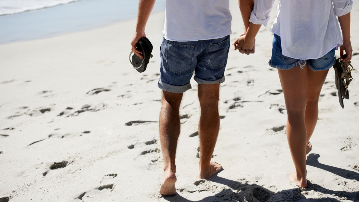 Two people walking hand in hand on a beach, representing connection without self abandonment.