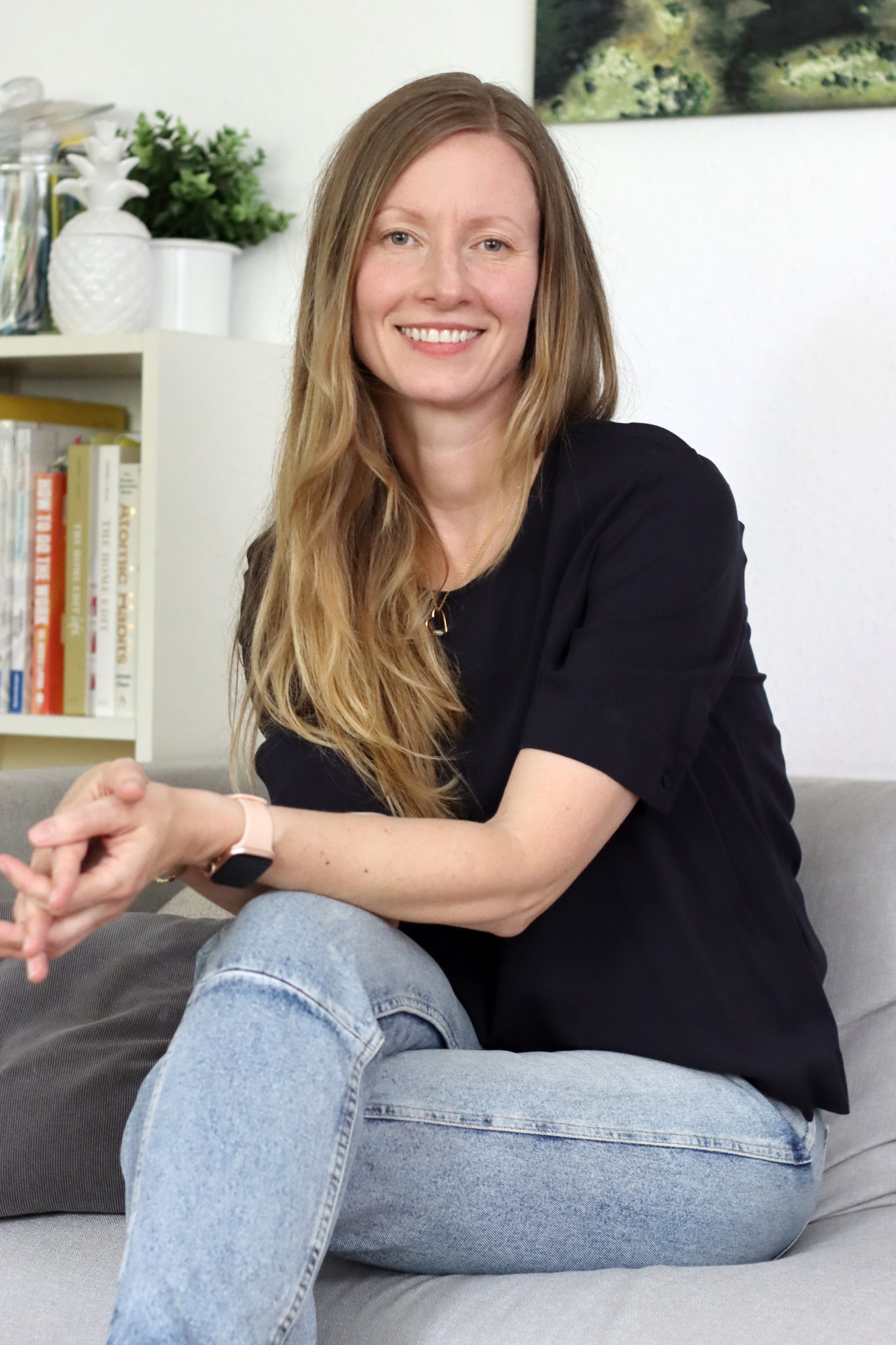 Dr. Julia Simon sitzt lächelnd auf einem Sofa. Neben ihr stehen Bücher in einem Regal