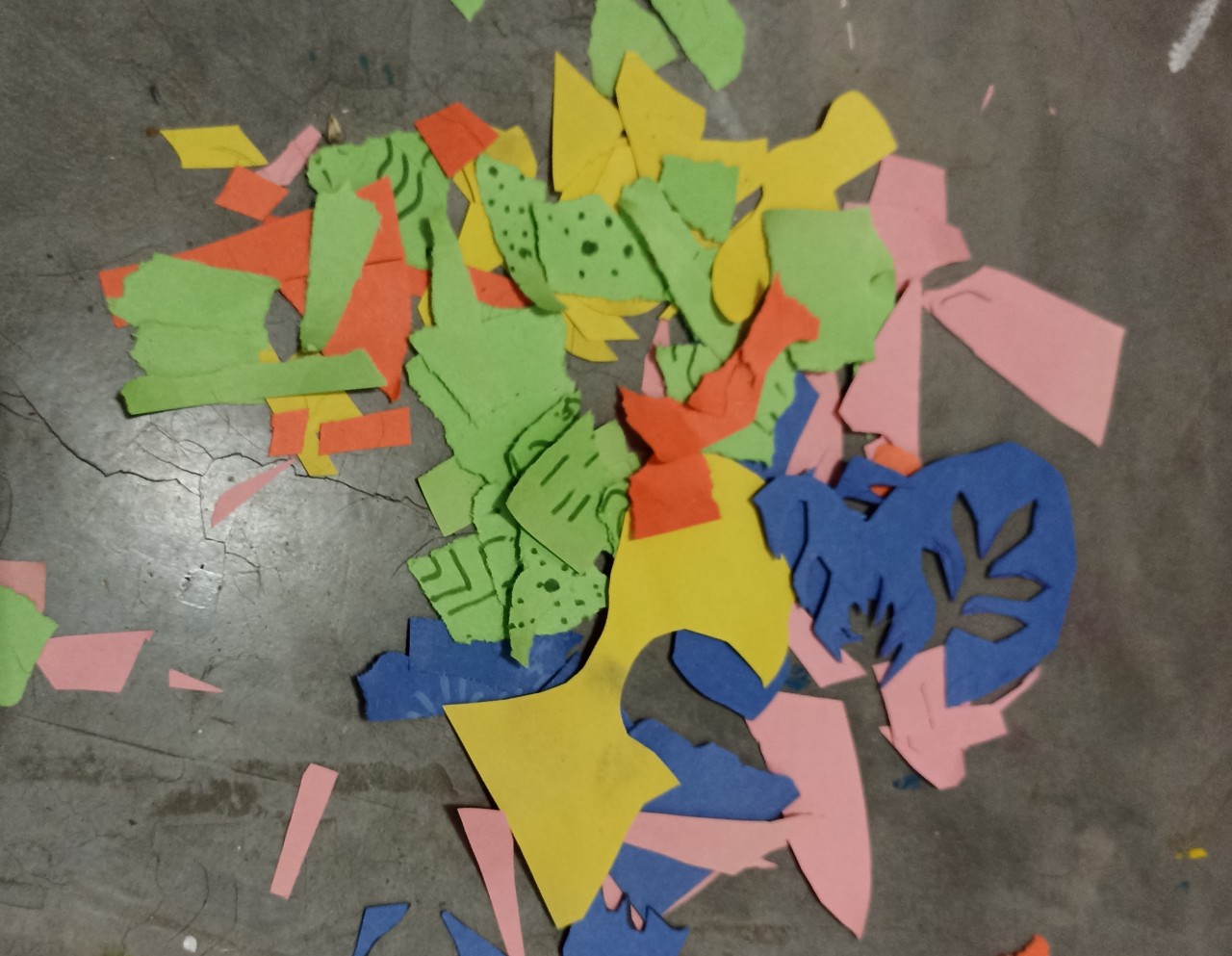 Loose pieces of colorful cut and torn paper scattered on a concrete floor