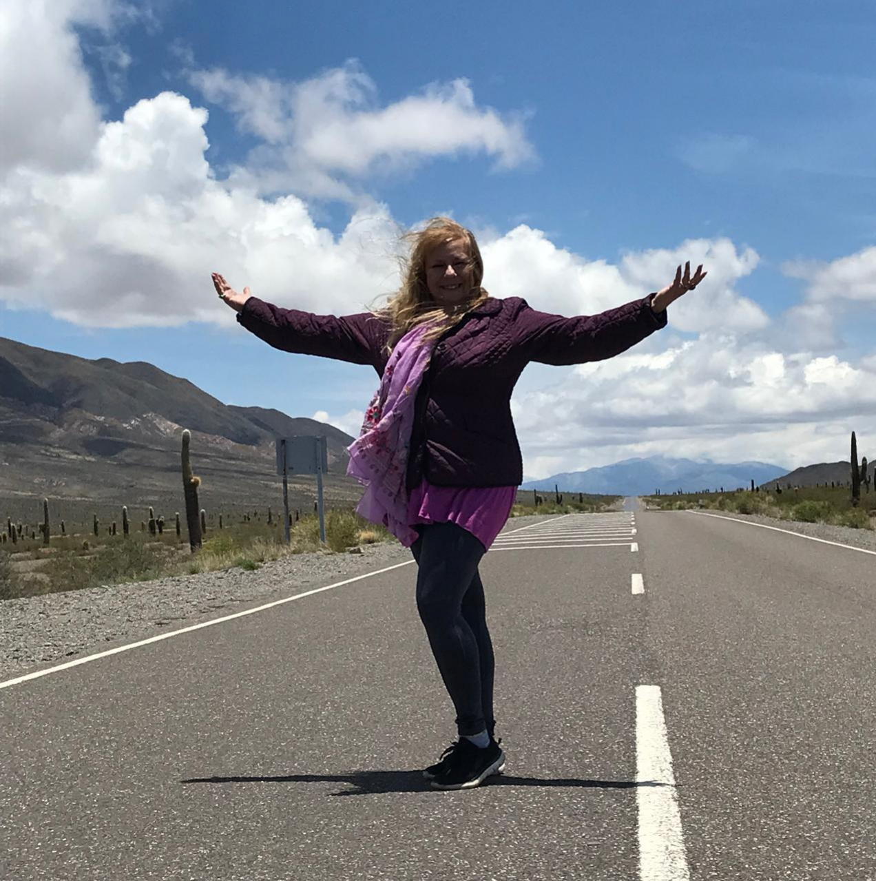 Encuentra tu libertad y bienestar emocional con los cursos de Mago Holístico Mujer con brazos abiertos en una carretera desierta rodeada de naturaleza, simbolizando libertad, bienestar holístico y la reconexión con uno mismo.