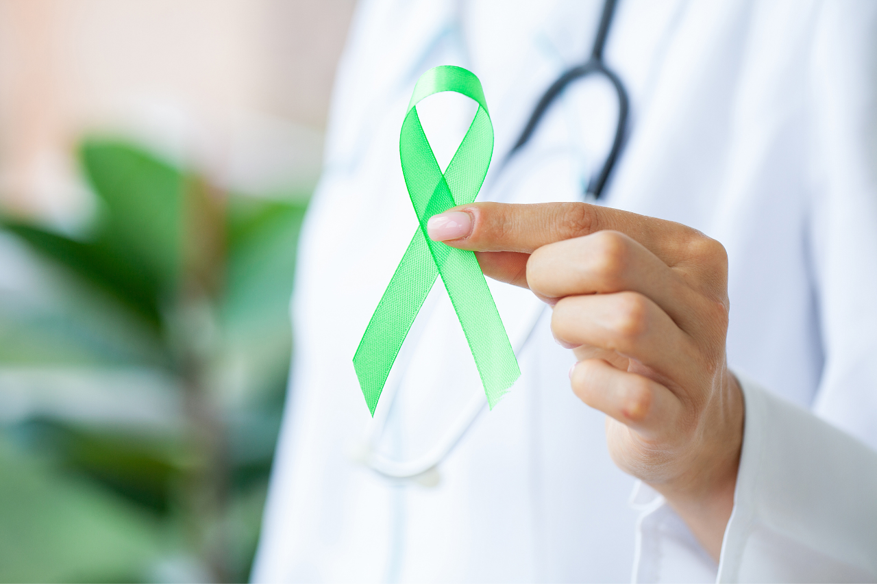 Mano sosteniendo un lazo verde, símbolo de la concienciación sobre la salud mental y el apoyo al bienestar emocional.