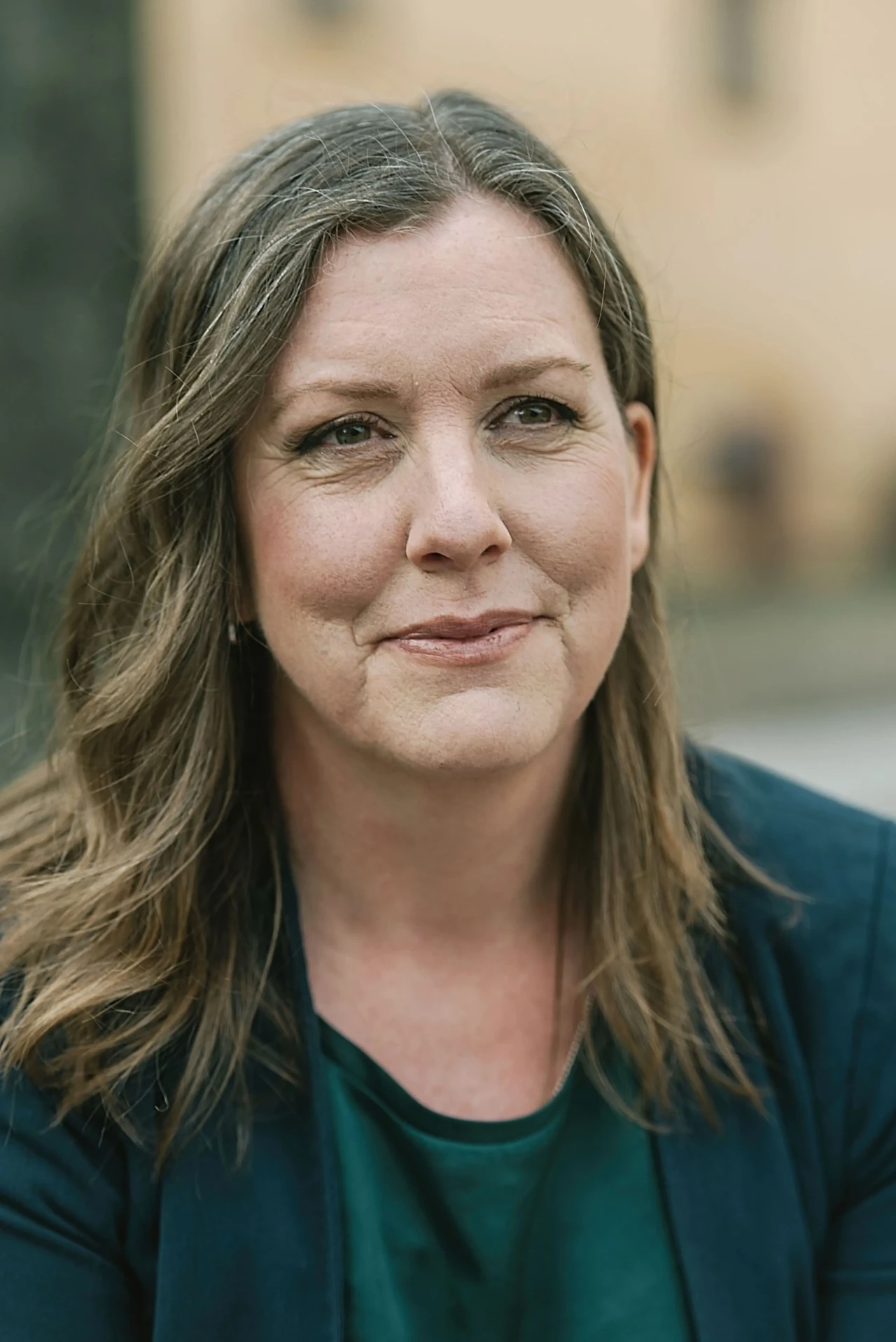 Anneli Olsson, författare och grundare av Storysmedjan Författaren Anneli Olsson klädd i blått och grönt har ljuset i ansiktet och kisar åt sidan