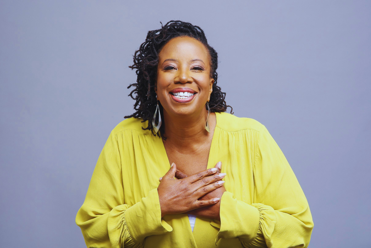 Black woman wearing a yellow dress, holding her hands over her heart