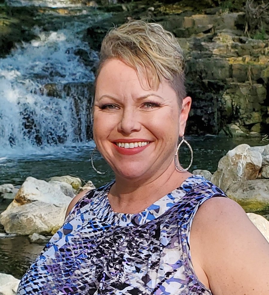 Kelly Riddle smiling warmly in front of a waterfall