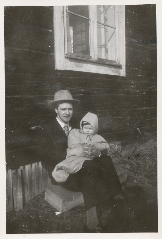 Svartvitt fotografi av Erling sittande utomhus med ett litet barn i famnen.