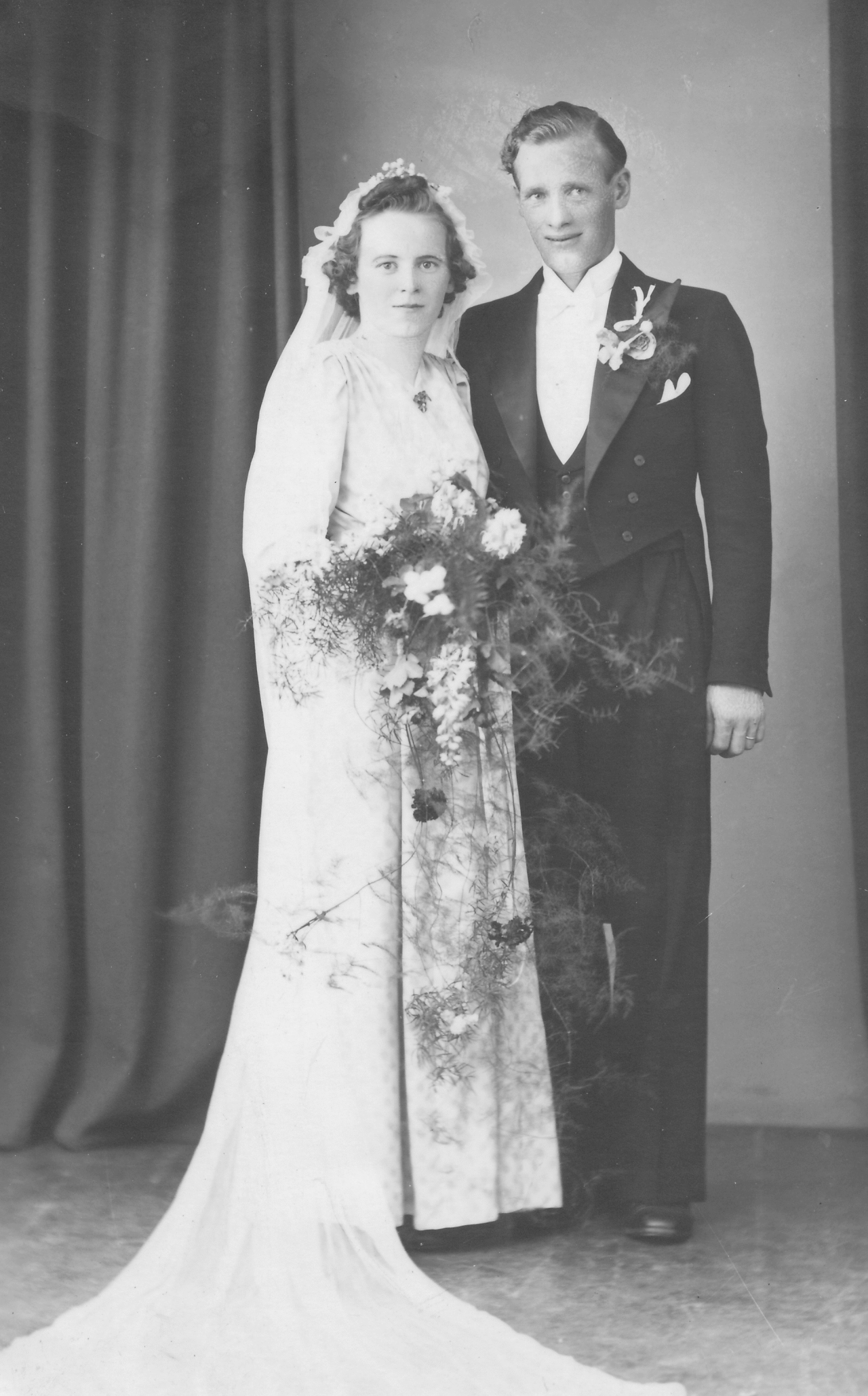 Svartvitt bröllopsfotografi av Eva och Emil, stående tillsammans med brudbukett och högtidskläder.