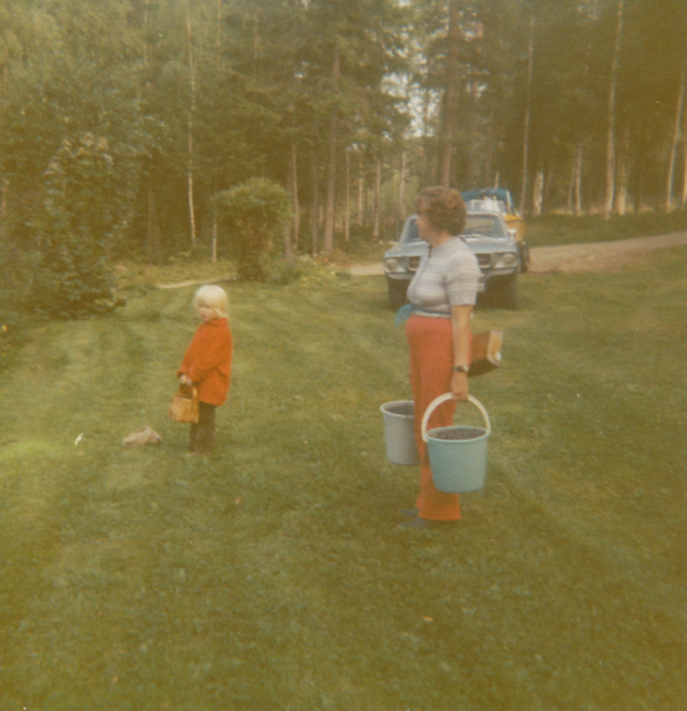 Färgfotografi av farmor Eva och barnbarnet Malin på väg hem från bärplockning med blåbärshinkar.