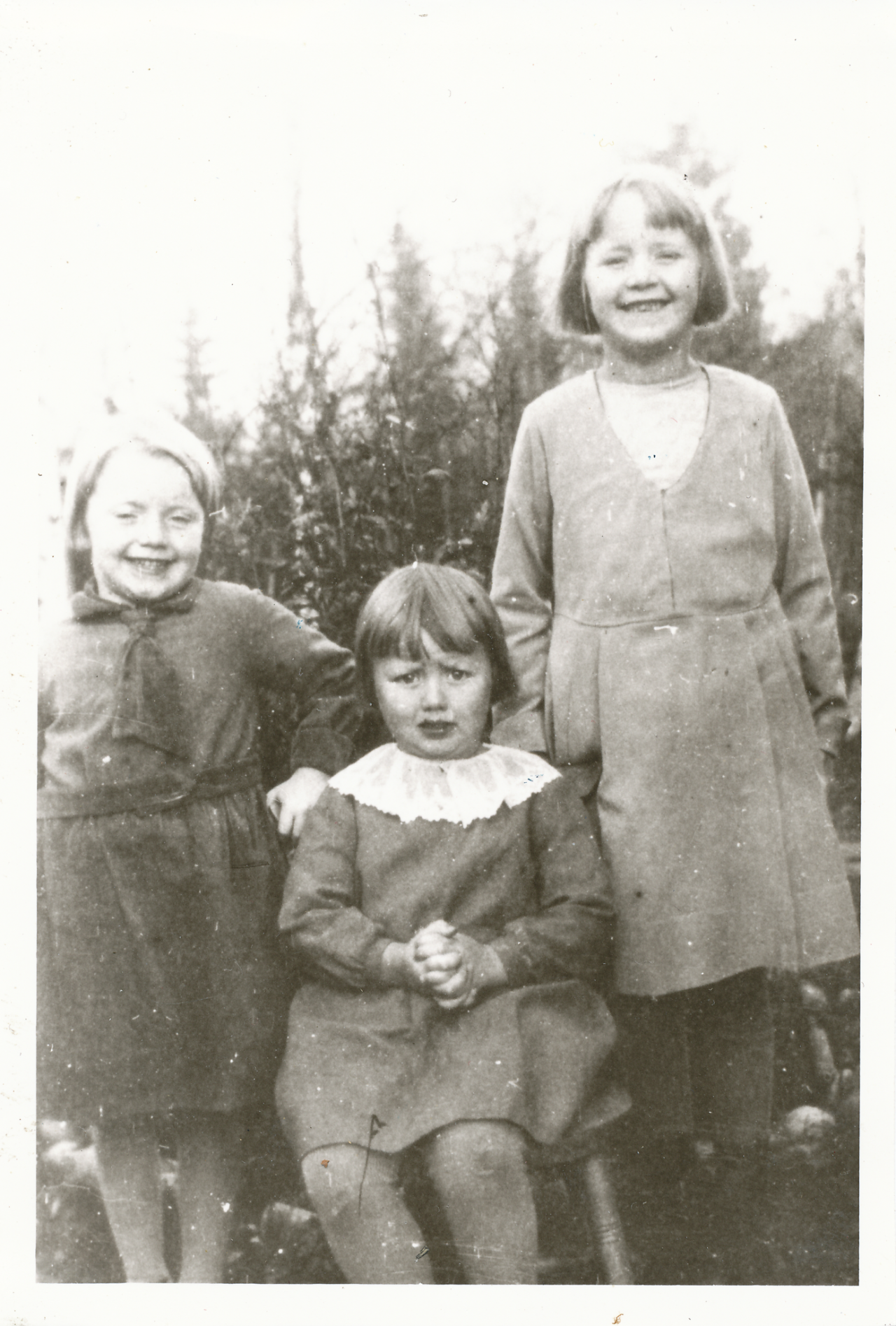 Svartvitt fotografi av tre flickor utomhus, där Mary står tillsammans med sina systrar.