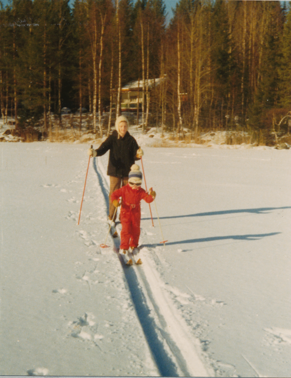 Färgfotografi av ett barn och en äldre kvinna på skidor i snötäckt landskap.