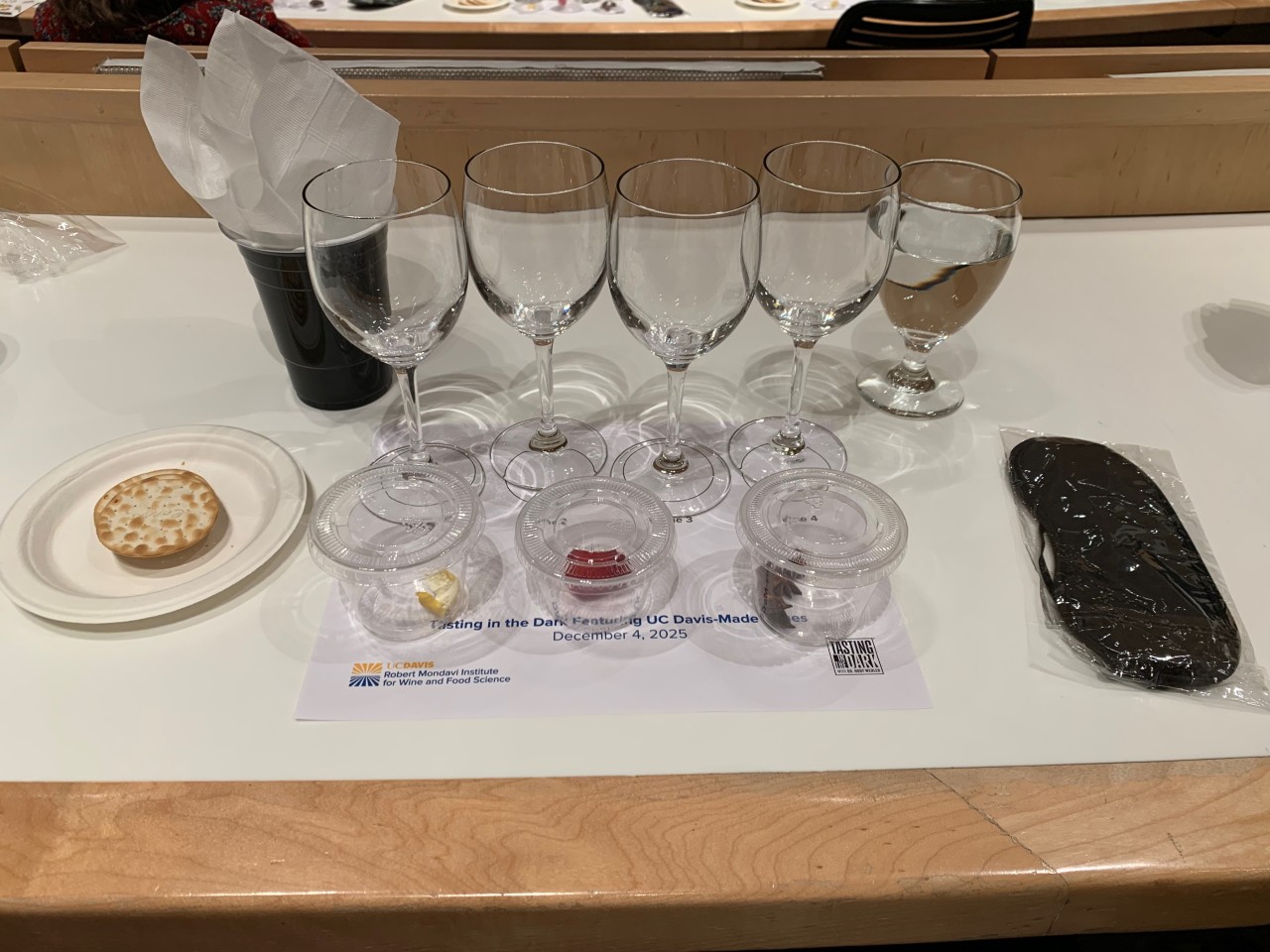 A photo of the tasting set showing: Four glasses. A spit cup. Crackers. A water glass. And three small sealed cups containing aroma references.