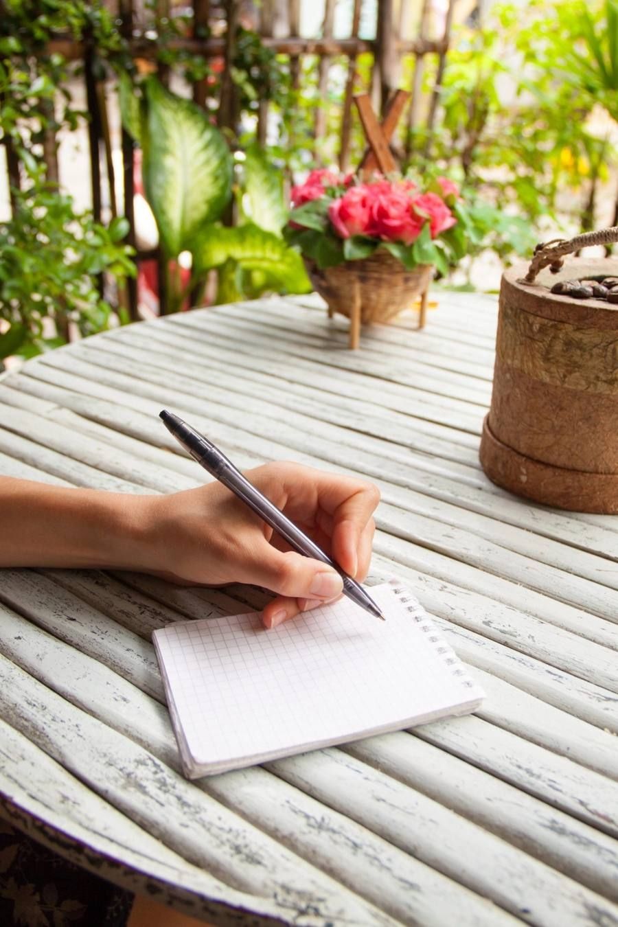 A hand writing revision notes in a notebook on a wooden table