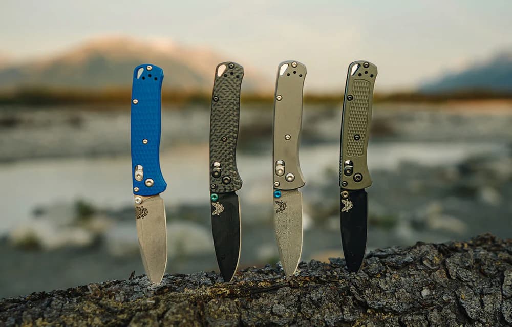 Four Benchmade Bugout folding knives lined up on a rock
