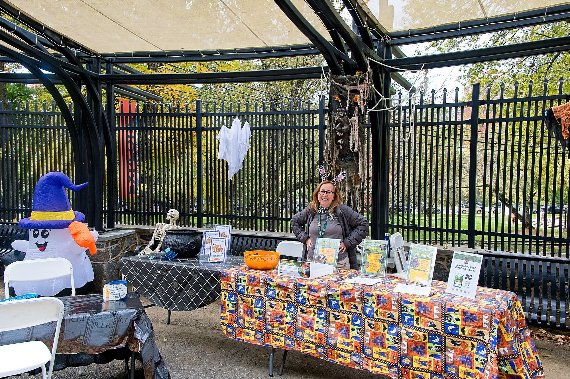 A volunteer docent stands behind a table with Halloween decorations and candy.