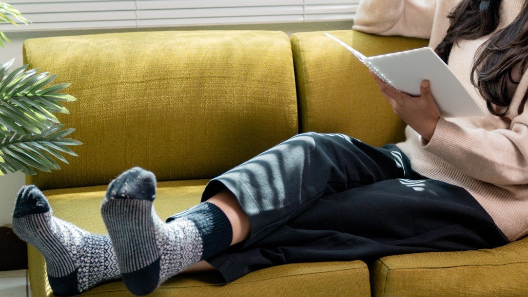 person on yellow couch reading with fuzzy socks on