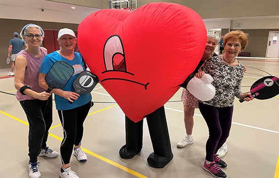 several pickleball players posed around someone in a heart costume