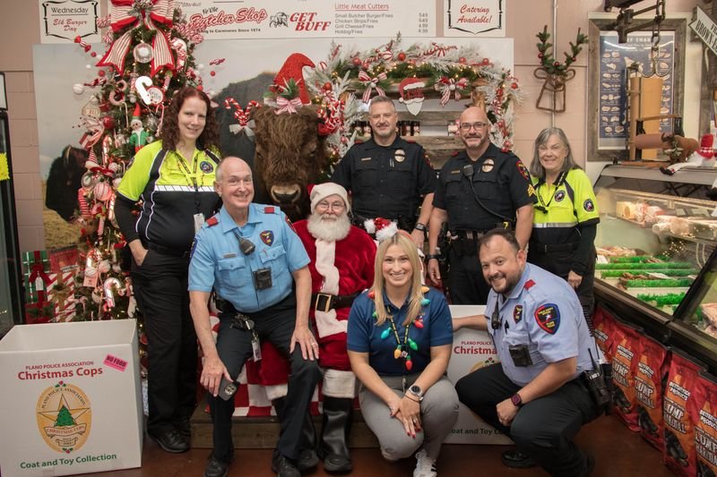 Festive decor and several police officers in uniform and other police department staff standing around Santa and a donation box