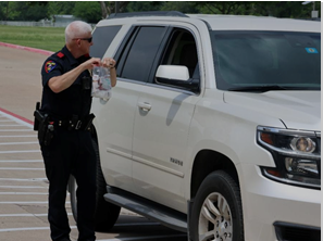 A police officer receives a container through an open car window in a drive-through for drug take back day